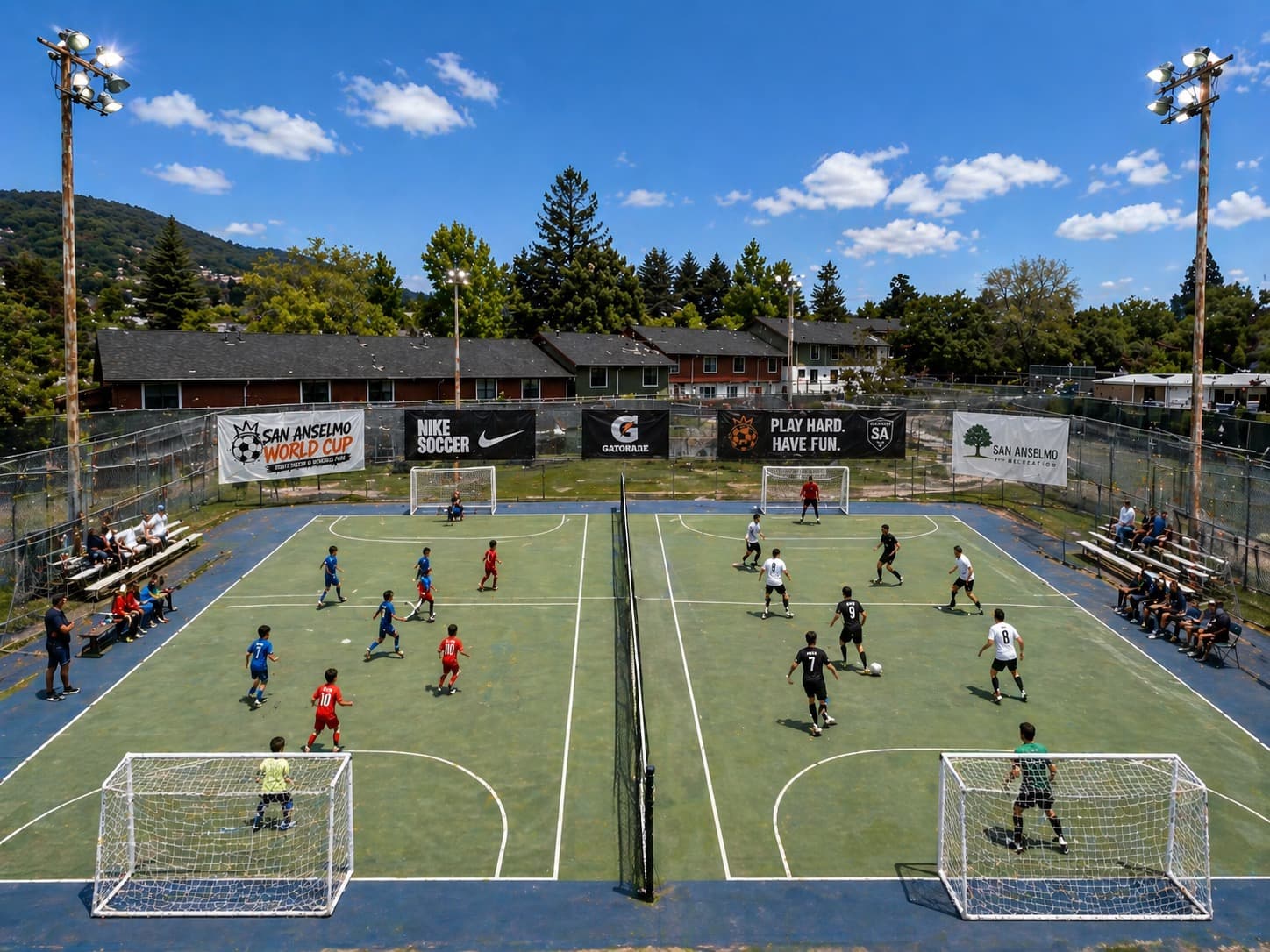 Aerial view of two side-by-side soccer pitches at Memorial Park, San Anselmo, with players mid-match and sponsor banners on the fences